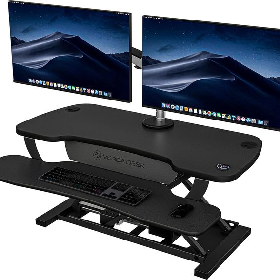 Black electric desk converter with a keyboard tray and two monitors placed on VESA mounts.