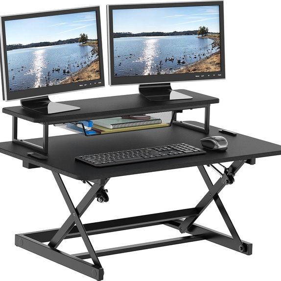 Black electric desk converter with a keyboard tray and two monitors placed on VESA mounts.