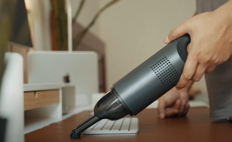 Person cleaning computer desk with a hand vacuum cleaner